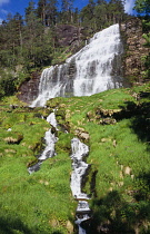 Norway, Rogaland, Svandalsfossen, Waterfall near town of Sauda.  White water flowing over tiered levels of rocks and through narrow  rocky gullys in foreground surrounded by trees and vegetation.