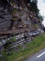 Norway, Troms, Landscape, Roadside rock face showing layering of materials shaped by glacial action and weathering.