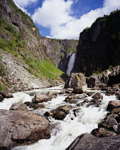 Norway, Hordaland, , Lower section of Voringsfossen waterfall cascading into steep sided valley gorge with river tumbling over rocks in foreground.
