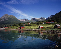Norway, Nordland, Holandsfjorden, Edge of Holansfjorden with red painted fishermen s huts and houses and mountain backdrop.