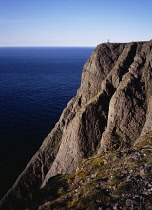Norway, Finnmark, Mageroya, Edge of Nordkapp  the most northerly road accessible point of Europe situated on the Isle of Mageroya.  Visitors silhouetted on cliff top and view over sea to horizon.