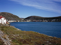 Norway, Finnmark, Nordkinnhalvoya, Fishing village of Kjollefjord overlooking water with eroded hillside behind.  Blue sky with thin  windswept cloud.