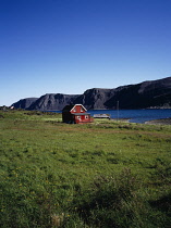 Norway, Finnmark, Nordkinnhalvoya, Red painted Summer farmhouse with white painted eaves and window frames beside Sandfjorden in area covered in deep snow during Winter.