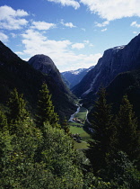 Norway, Hordaland, Naeroydalen, View east from near village of Stalheim over steep sided river valley with small clusters of buildings framed by tree tops in foreground.
