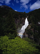 Norway, Hordaland, Naeroydalen, Stalheimfossen.  White waterfall crashing down steep sided cliff disected by rainbow with lush  green ferns in foreground.