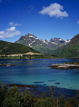 Norway, Lofoten, Indrefjorden, View across dark turquoise water of fjord with peak of Porselvtinden Mountain behind criss-crossed with lines of snow and cloud shadow.