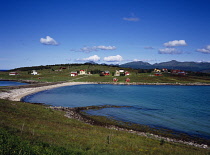 Norway, Lofoten, Hadsel Island, Village of Hanoyvika.  Red  cream and white painted houses overlooking bay with mountain backdrop.