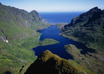 Norway, Lofoten, Moskenesoya Island, View east over Agvatnet Lake with Andstabben Mountain on right hand side and Vestfjorden beyond.  Steep granite rockface with trees scattered across lower slopes.