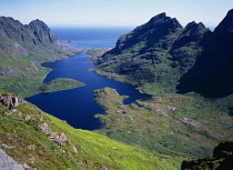 Norway, Lofoten, Moskenesoya Island, View east over Agvatnet Lake with Andstabben Mountain on right hand side and Vestfjorden beyond.  Steep granite rockface with trees scattered across lower slopes.
