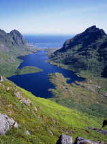 Norway, Lofoten, Moskenesoya Island, View east over Agvatnet Lake with Andstabben Mountain on right hand side and Vestfjorden beyond.  Steep granite rockface with trees scattered across lower slopes.