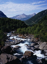 Norway, Nordland, Fykanaga River, River flowing west from the Glomfjord Mountains across rocks and boulders through tree lined valley.