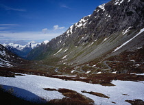 Norway, Sogn og Fjordane, Videdalen, Looking west along winding road at foot of mountains part covered with snow.