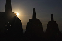 Indonesia, Java, Borobudur, Silhouetted stupas soon after dawn, with sun peeking round one of them