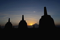 Indonesia, Java, Borobudur, Three stupas silhouetted against the sun rising behind the volcano, Mount Merapi.