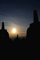 Indonesia, Java, Borobudur, Stupas silhouetted against newly risen sun behind volcano, Mount Merapi
