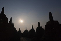 Indonesia, Java, Borobudur, Two rows of stupas silhoutted against the morning sun.