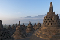 Indonesia, Java, Borobudur, Stupas in the early-morning warm glow, with misty countryside and forested hills in the background