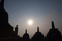 Indonesia, Java, Borobudur, Stupas and child visitor silhouetted against the morning sun.