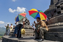 Indonesia, Java, Borobudur, Local man, shaded by a multi-coloured umbrella, pauses on the main stupa in the midday heat.