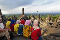 Indonesia, Java, Borobudur, A group of very colourfully dressed, seated Muslim women look out over the monument to the surrounding countryside.
