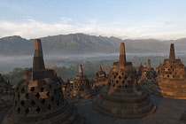 Indonesia, Java, Borobudur, Early-morning, misty view across stupas and the countryside to volcano, Mount Merapi
