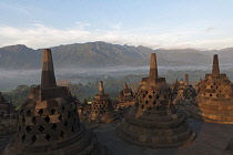 Indonesia, Java, Borobudur, Early-morning, misty view across stupas and the countryside to volcano, Mount Merapi