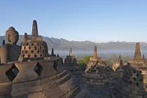 Indonesia, Java, Borobudur, Seated Buddha and small stupas on the top level, with misty valley and forested hillsides in the background