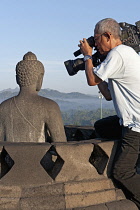 Indonesia, Java, Borobudur, Cameraman filming close-up of one of the seated Buddhas on the top level