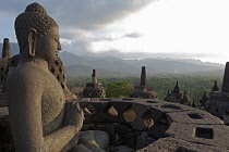 Indonesia, Java, Borobudur, Seated Buddha looking out over stupas and the surrounding forested hills and countryside