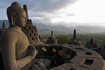 Indonesia, Java, Borobudur, Seated Buddha looking out over stupas and the surrounding forested hills and countryside