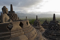 Indonesia, Java, Borobudur, Seated Buddha looking out over stupas and the surrounding forested hills and countryside