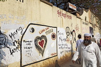 India, Maharashtra, Mumbai, Muslim man walking past an 'art wall' covered with upbeat, positive slogans and images, with the theme Long Live Mumbai.