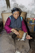 India, West Bengal, Darjeeling, Senior Tibetan woman, in traditional clothing, carding sheeps' wool in Tibetan Self-help Refugee Centre.