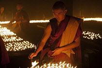 India, Bihar, Bodhgaya, Buddhist monk lighting merit-making candles in the grounds of the Mahabodhi Temple.