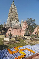 Marigold flowers in the shape of an Indian swastika in the foreground, with the Mahabodhi Temple in the background