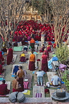 Bihar; Bodhgaya; Mahabodhi Temple; South Asia;In background a large group of Buddhist monks are seated, waiting for a prayer ceremony at the Mahabodhi Temple; in the foreground, Buddhist devotees do t...