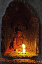 Nepal, Kathmandu, Small, candle-lit niche in the shrine to Ajima, goddess of smallpox, containing an ancient, seated Buddha, blacked by candle soot, and decorated with red powder, with rice grains and...