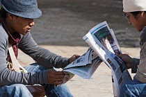 Nepal, Kathmandu, Two teenage Nepali males reading newspapers opposite each other in the shadow of the Great Stupa.