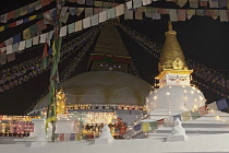 Nepal, Kathmandu, Night view of the Great Stupa and a mini-stupa in front of it decorated with coloured lights in celebration of a full moon.