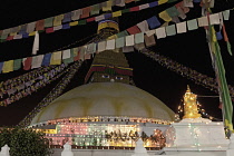 Nepal, Kathmandu, The Great Stupa seen at night, framed by Buddhist prayer flags and decorated with multi-coloured lights in celebration of a full moon.