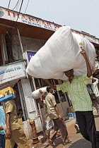 India, Maharashtra, Mumbai, Local man carrying large plastic sack on his head in a street in Crawford Market.