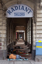 India, Maharashtra, Mumbai, Homeless people asleep on the pavement in an arcade of shops, beneath a sign saying 'Radiant Tailors', Colaba.