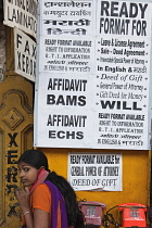 India, Maharashtra, Mumbai, Teenage girl on the phone beneath a sign advertising a variety of ready-made documents available at a stationery shop.