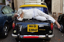 India, Maharashtra, Mumbai, Taxi driver fast asleep on the boot of his car.