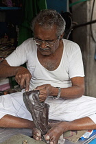 India, Maharashtra, Mumbai, Traditional pavement cobbler repairing leather shoes by hand in central Bombay.