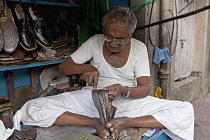 India, Maharashtra, Mumbai, Traditional pavement cobbler repairing leather shoes by hand in central Bombay.