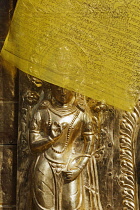 Nepal, Kathmandu, Small brass statue of a standing Buddha with face partially obscured by a yellow Buddhist prayer flag, Swayambhunath temple Monkey Temple.