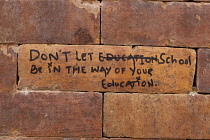 Nepal, Kathmandu, Brick in a wall with Don't Let School Be In The Way of Your Education written on it.