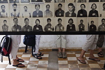 Cambodia, Phnom Penh, Western tourists lower legs and feet visible beneath a display of victims' photo portraits at Toul Sleng Genocide Museum S-21. Toul Sleng was a high school, taken over by the Khm...