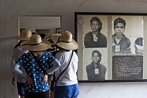 Cambodia, Phnom Penh, Tour group looking at victims' portraits, Toul Sleng Genocide Museum S-21. Toul Sleng was a high school, taken over by the Khmer Rouge and turned into a prison, where people were...